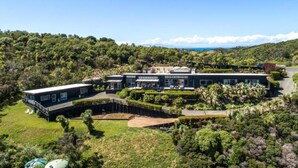 Un edificio moderno de dos pisos con una amplia fachada de vidrio, rodeado de exuberante vegetación y vistas al océano.