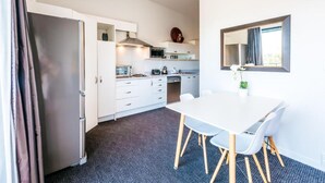 Una cocina moderna con gabinetes blancos, un microondas y una estufa. Hay un comedor con una mesa y sillas blancas.