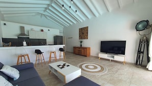 A modern living room with a sofa, a coffee table, a TV, and a kitchen in the background.