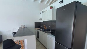A modern kitchen with a black refrigerator, white cabinets, and a dining area with a black chair and a small table.