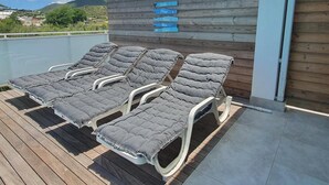 A deck with four grey cushioned lounge chairs and a wooden wall with a sign indicating 'Salas' and 'Plazas'.