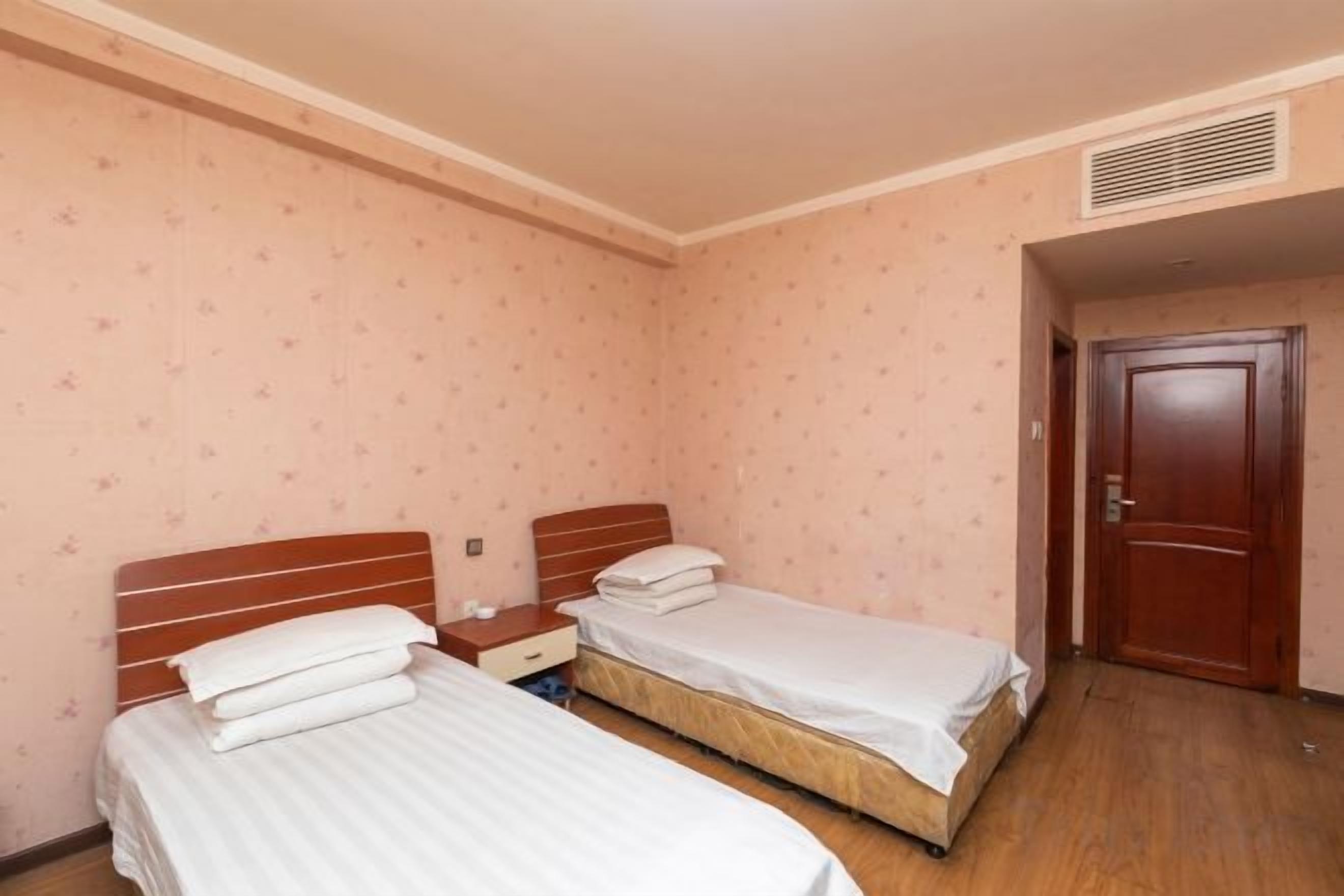 Una habitación con dos camas individuales, piso de madera y una puerta.