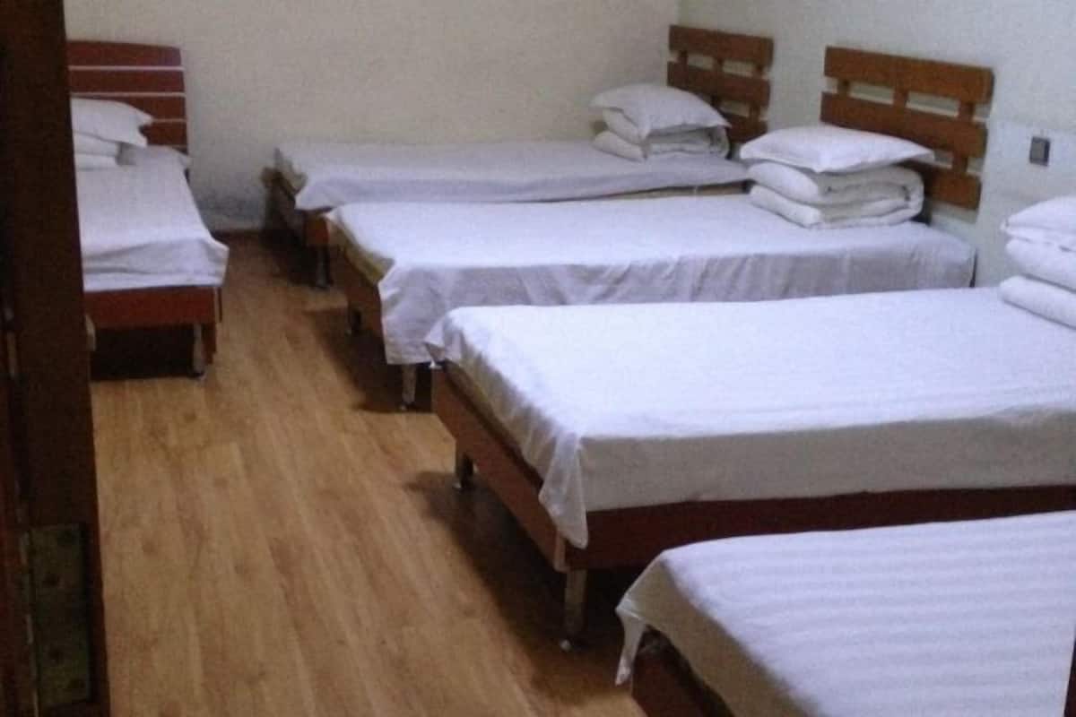 Ein Zimmer mit vier Einzelbetten, die in einer Reihe angeordnet sind, Holz-Kopfteilen und Holzboden.