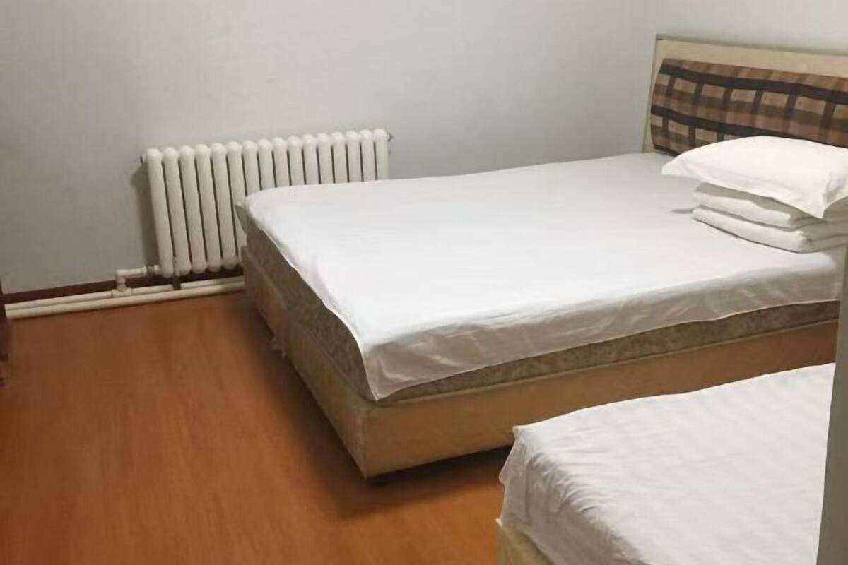 Ein Einzelbett mit weißer Matratze und Kissen, ein Heizkörper und Holzboden.