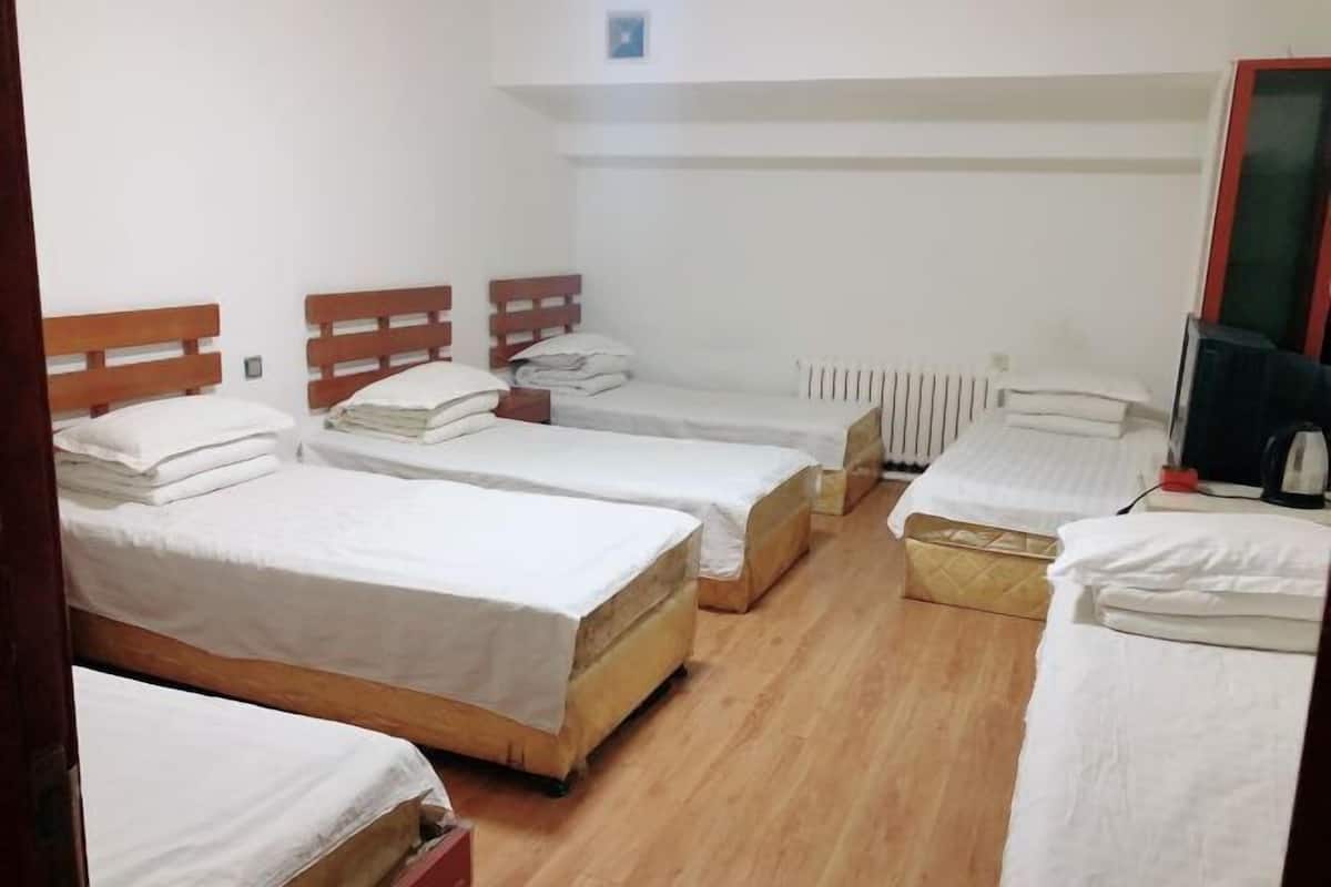 Ein Zimmer mit vier Einzelbetten, Holz-Kopfteilen, weißer Bettwäsche, einer Heizung und einem Fernseher.