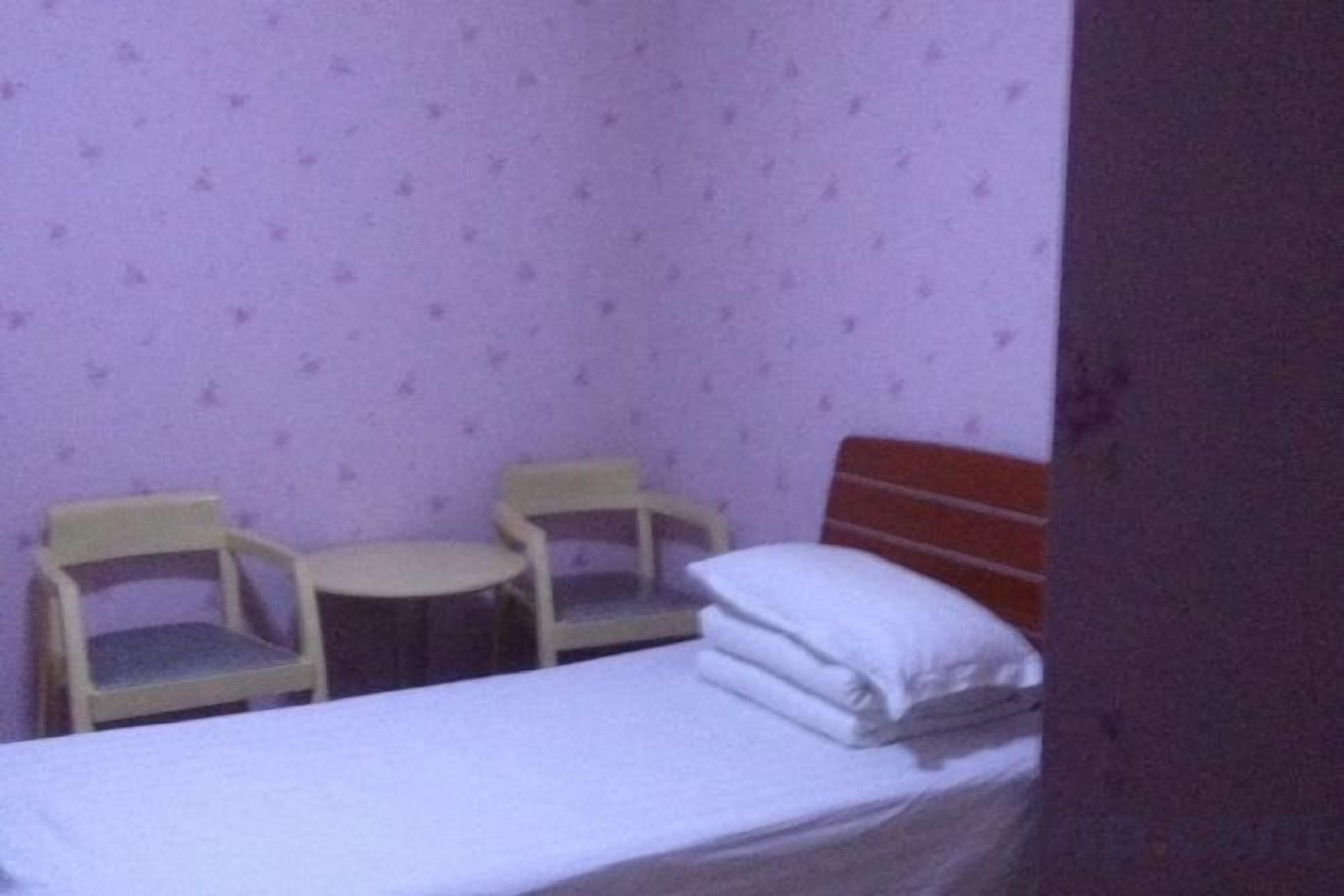 Una habitación pequeña con una cama, dos sillas y una mesita.