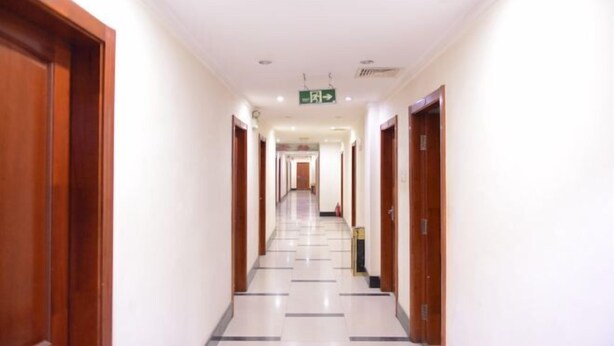 A hotel corridor with wooden doors, a tiled floor, and a green exit sign. - Harbin Summer Hotel (Harbin)