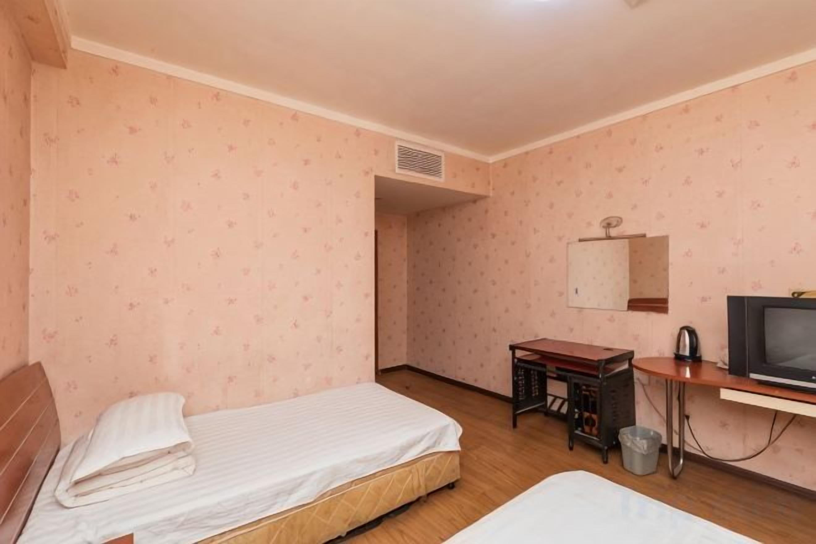 A small room with two beds, a desk, a television, and a mirror.