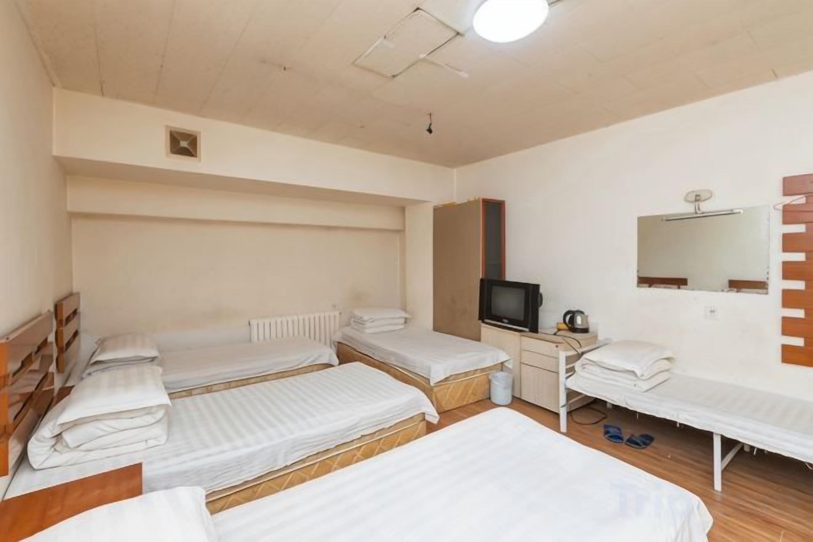 Habitación de hotel con cuatro camas individuales, un escritorio con televisor, un espejo y un radiador.