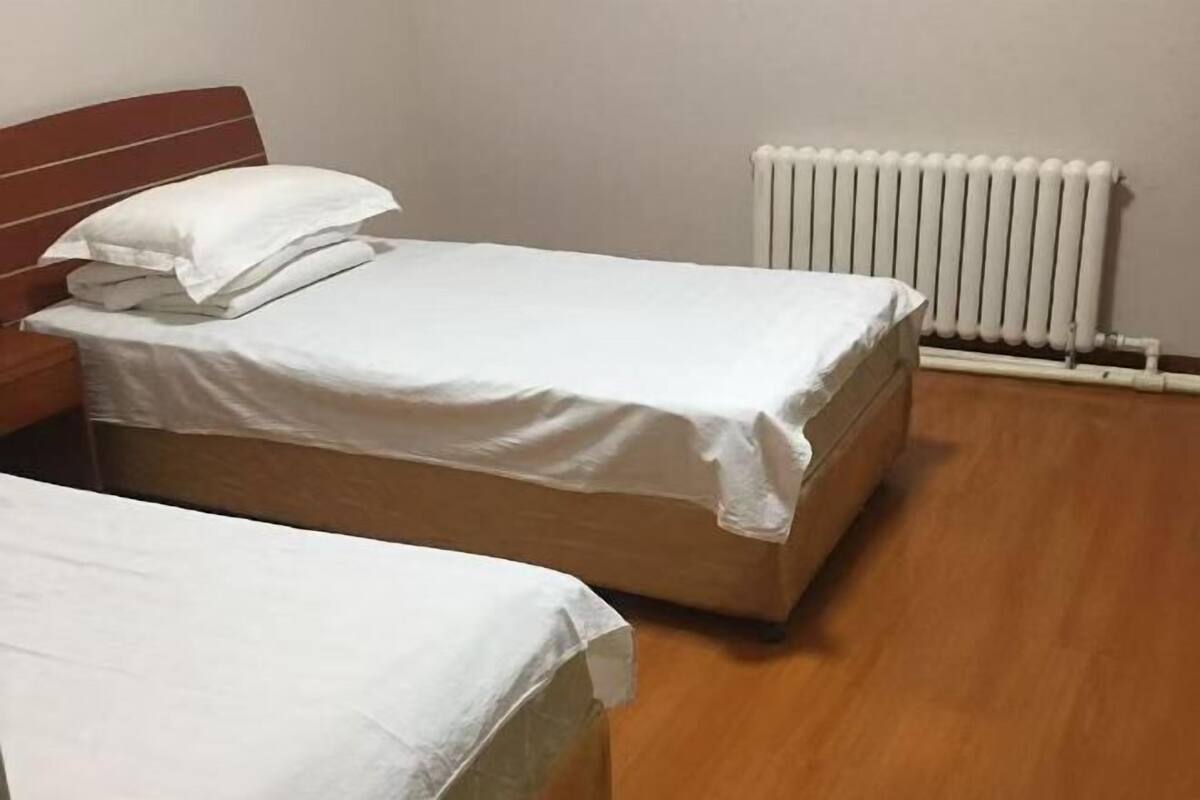 Ein Einzelbett mit Holz-Kopfteil und weißer Bettwäsche in einem Zimmer mit Heizkörper und Holzboden.