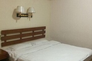 Una cama individual con cabecera de madera, dos lámparas fijadas a la pared y una mesita de noche.
