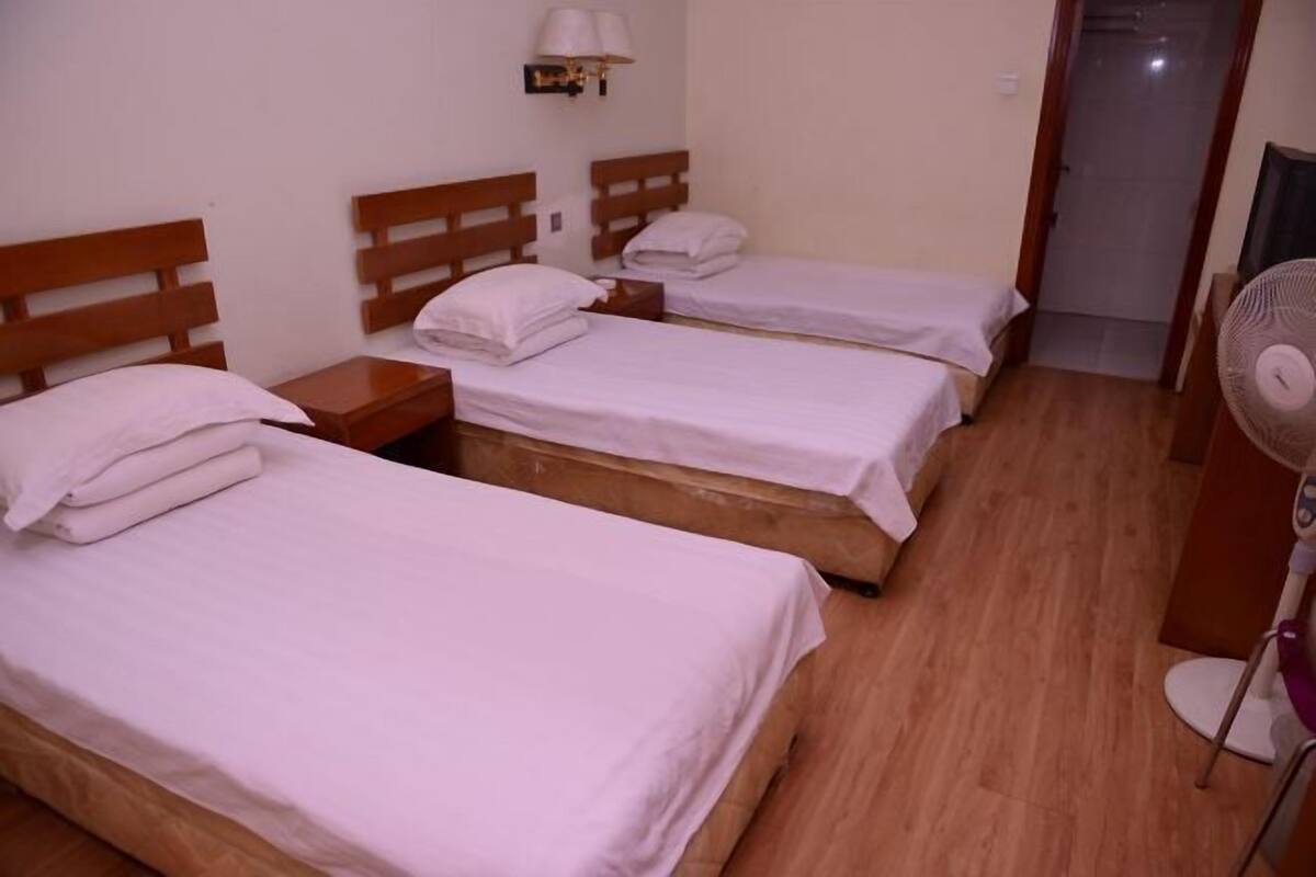 Ein Hotelzimmer mit drei Einzelbetten, Holz-Kopfteilen, Nachttischen und einer Wandlampe.