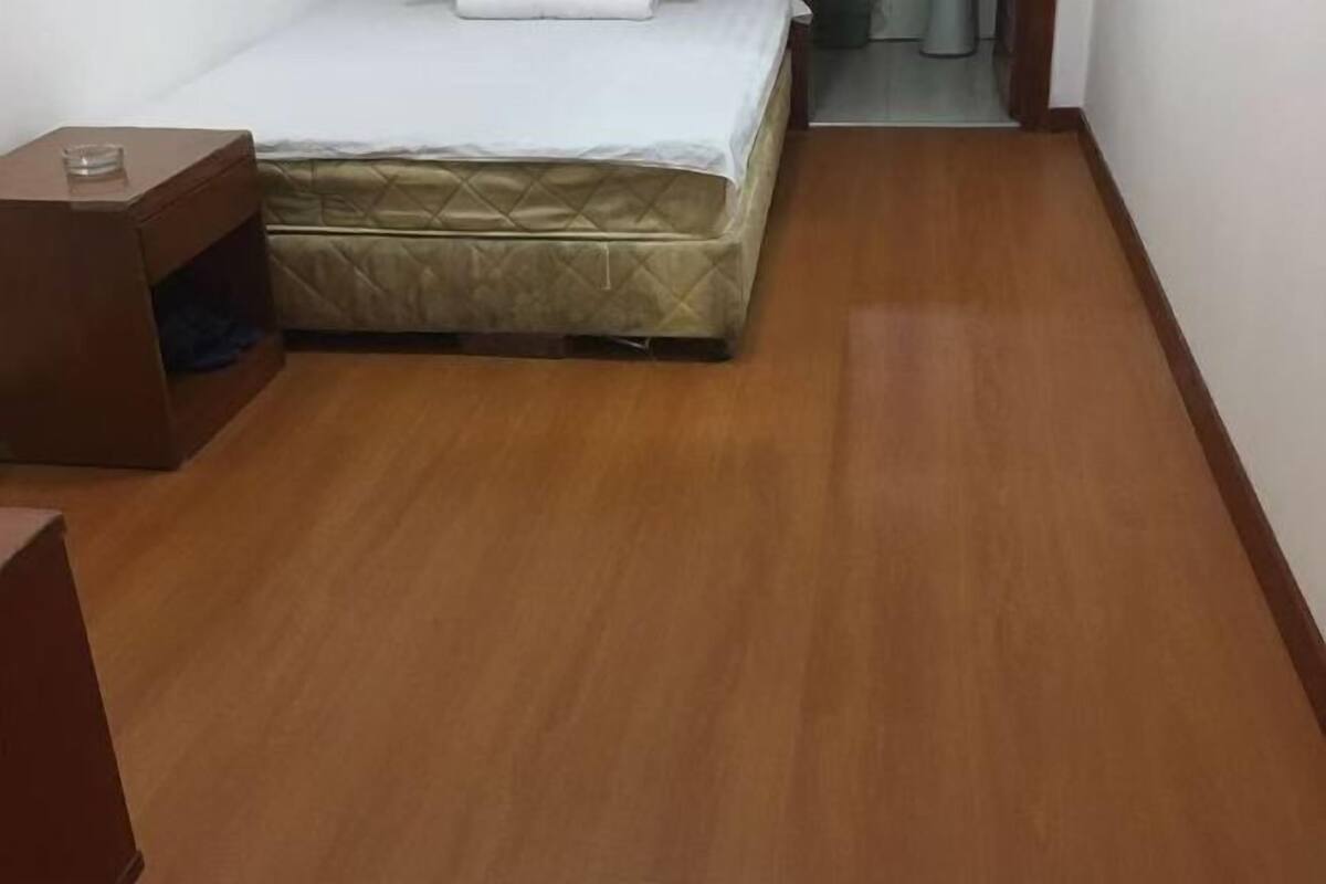 Ein Zimmer mit einem Bett, einem Nachttisch aus Holz und einer Tür zu einem weiteren Raum.
