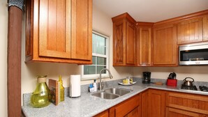 A kitchen with wooden cabinets, granite countertops, a stainless steel sink, a microwave, and a window. - Casita Rojo - historic duplex in the heart of downtown Paso Robles (Paso Robles)