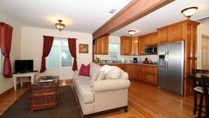 A living room with a sofa, a coffee table, and a television. The room has wooden flooring and a kitchen area with a refrigerator and microwave. - Casita Rojo - historic duplex in the heart of downtown Paso Robles (Paso Robles)