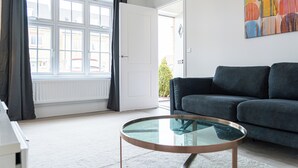 A modern living room with a dark grey sofa, a glass coffee table, and a large window with curtains. - 3 Bedroom, 3.5 Bathroom House, Goodwood, Chichester (Chichester)