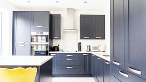 A modern kitchen with dark cabinets, stainless steel appliances, and a yellow chair. - 3 Bedroom, 3.5 Bathroom House, Goodwood, Chichester (Chichester)