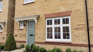 A brick building with a green door, white windows, and a small garden area with shrubs. - 3 Bedroom, 3.5 Bathroom House, Goodwood, Chichester (Chichester)