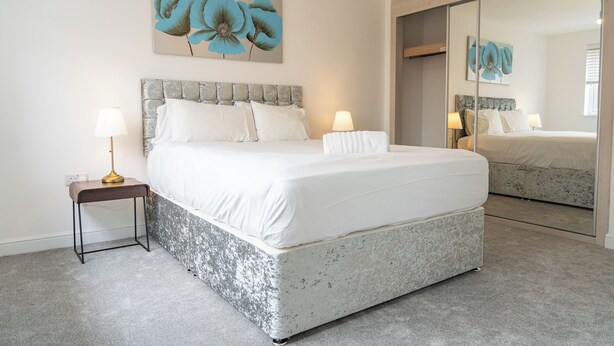 A bedroom with a large bed, two bedside tables with lamps, a large mirror, and a floral artwork on the wall. - 3 Bedroom, 3.5 Bathroom House, Goodwood, Chichester (Chichester)