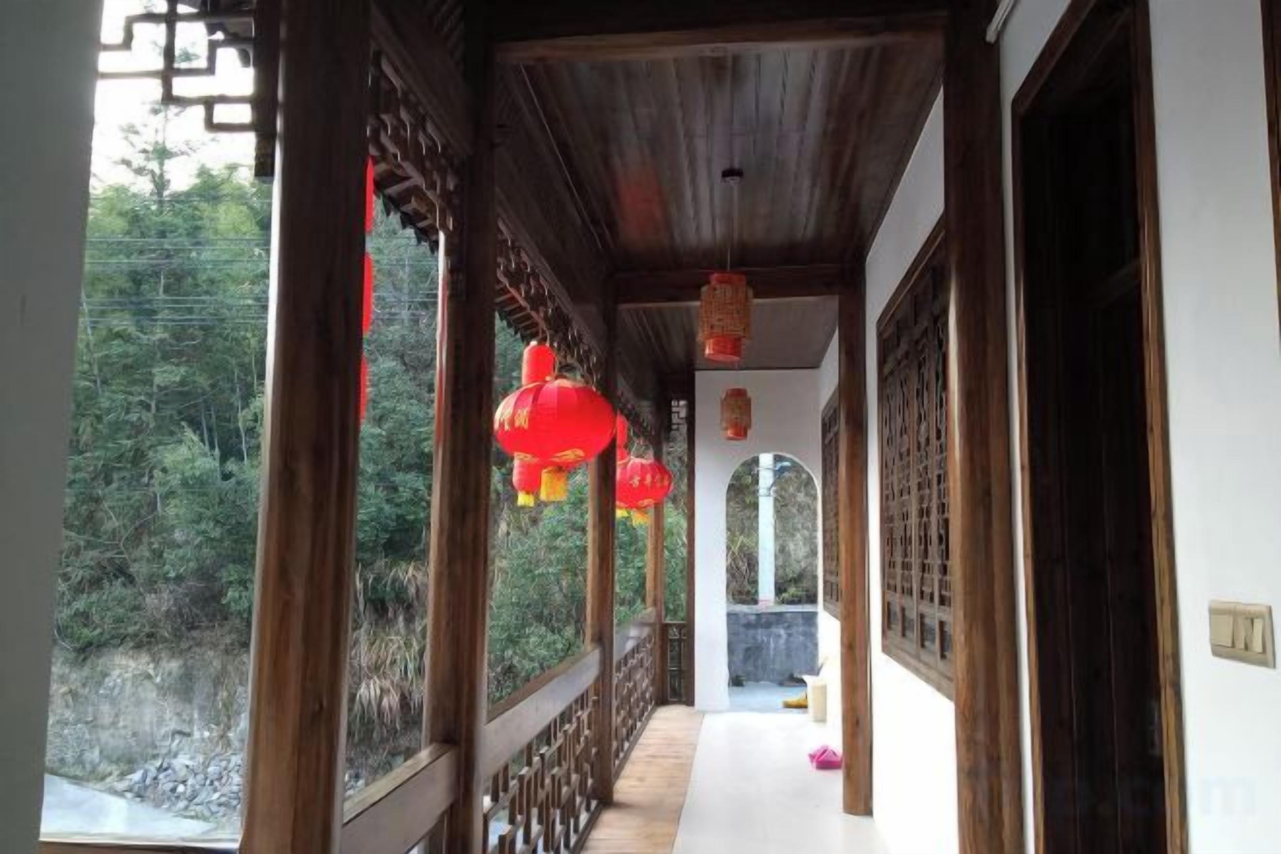 A corridor with wooden railings and red lanterns, leading to a door with a traditional lattice design.