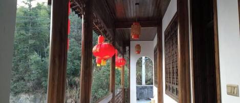 A corridor with wooden railings and red lanterns, leading to a door with a traditional lattice design.