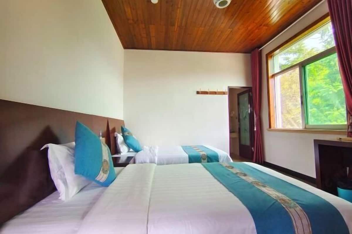 Habitación de hotel con dos camas, techo de madera, ventana grande con cortinas y un pequeño escritorio.