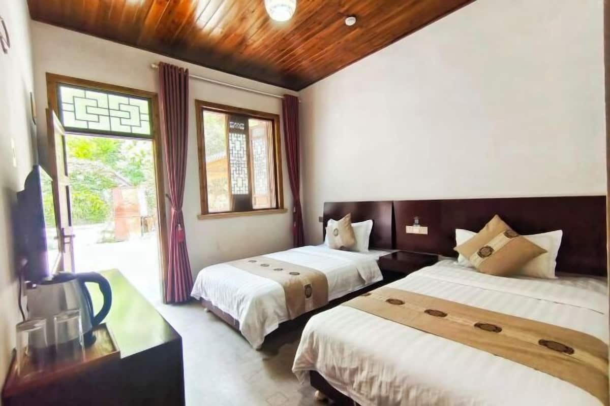Habitación de hotel con dos camas, techo de madera y ventana con cortinas.