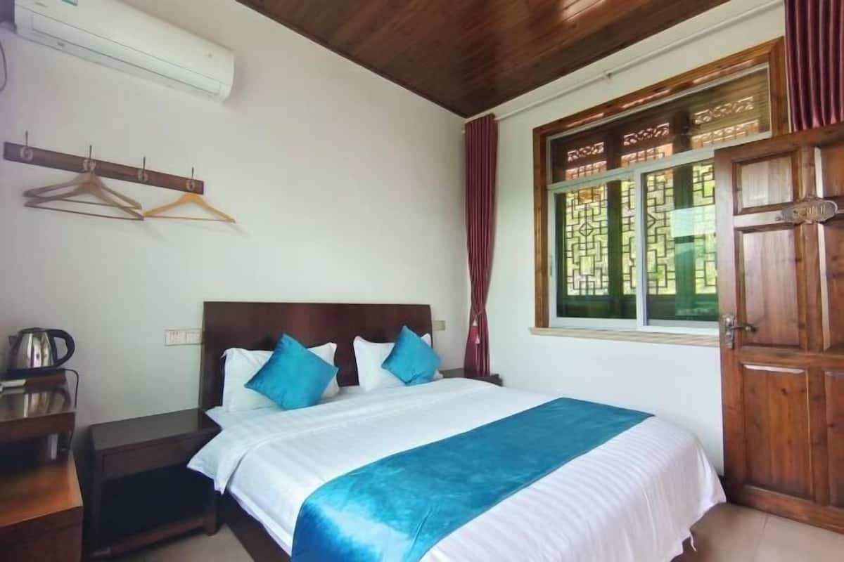 Un dormitorio con cama, cabecera de madera, ventana con cortinas y una puerta de madera.