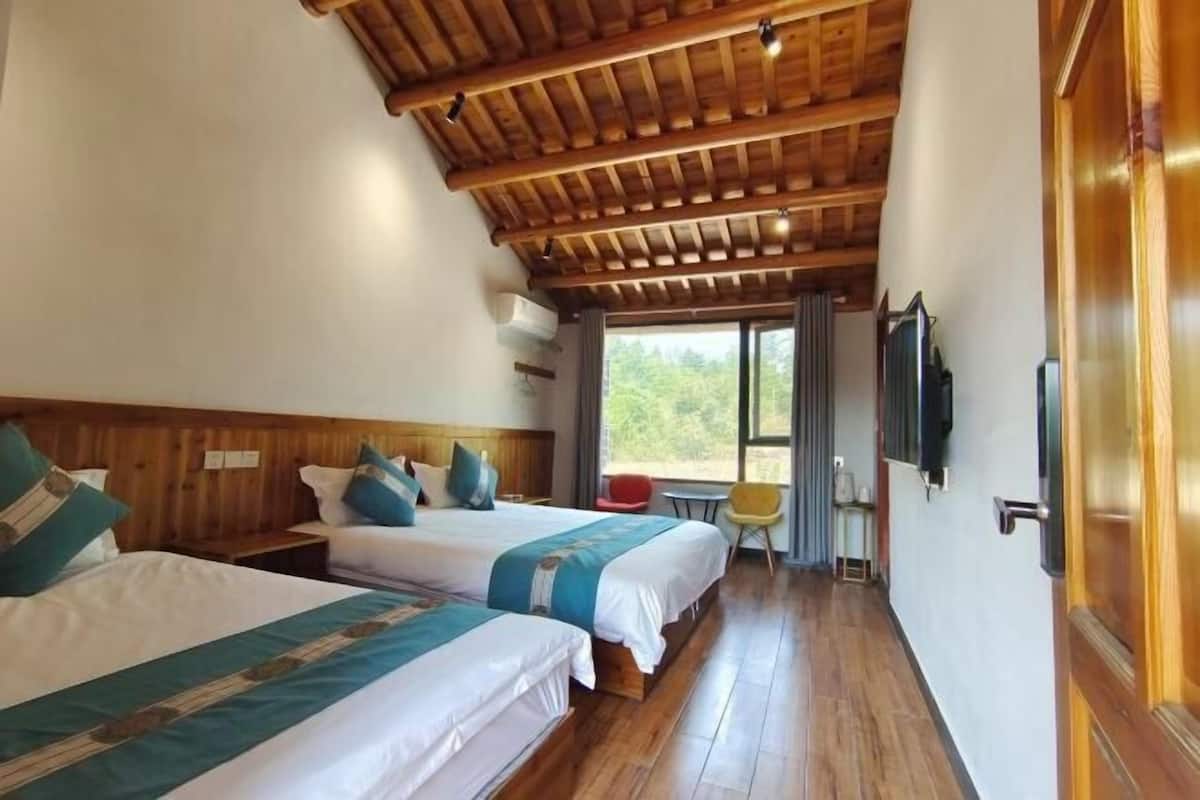 Habitación de hotel con dos camas, vigas de madera en el techo, un ventanal grande y un televisor en la pared.