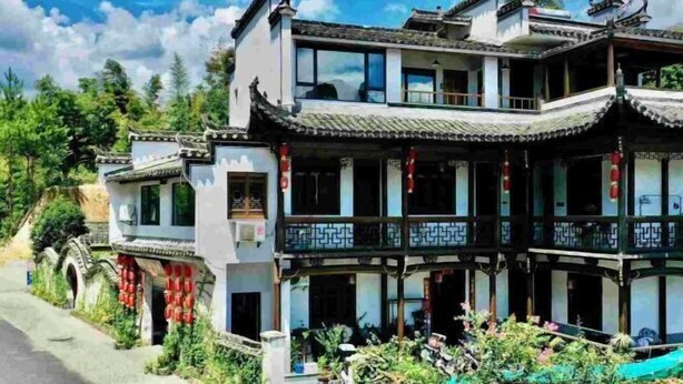 A traditional multi-story building with a balcony, surrounded by greenery and a clear sky. - yi xian hong cun Yue han bo Inn (Yi County)