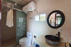 Kylpyhuone, jossa on wc, koristeellisella altaalla varustettu pesuallas, peili ja suihkutila.