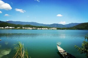 Un lago tranquilo con un bote de madera amarrado en la orilla, rodeado de montañas y edificios al fondo.