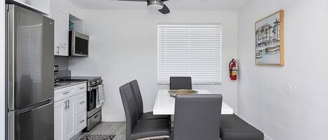 Una cocina compacta con electrodomésticos modernos, un comedor con mesa y sillas, y un ventilador de techo.