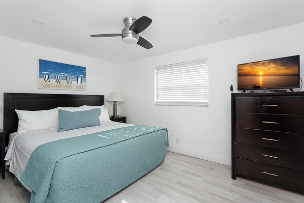 A bedroom with a bed, a ceiling fan, a TV on a dresser, and a painting of a beach scene. - ULTRA relaxing 2 bed beach&boardwalk apt (Hollywood)
