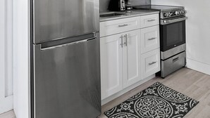 Uma cozinha moderna com eletrodomésticos de aço inoxidável, armários brancos e um tapete estampado.