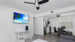 Uma sala de estar moderna com televisão de tela plana, mesa de centro branca, sofá cinza e ventilador de teto.