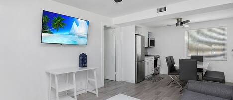 A modern living room with a flat-screen TV, a white coffee table, a gray sofa, and a ceiling fan.