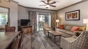 Habitación de hotel con comedor, sofá, televisor y balcón con cortinas.