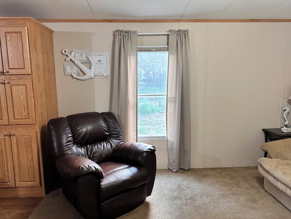 A room with a brown leather chair, a beige sofa, a wooden cabinet, and a window with curtains.