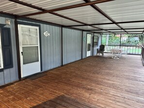 A covered porch with a wooden floor, a door, and a table with chairs.