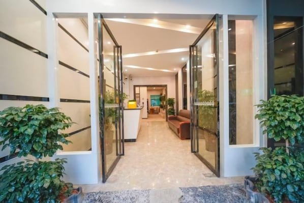 Un vestíbulo de hotel con puerta de cristal, mostrador de recepción y zona de estar.