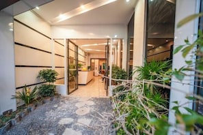 A modern reception area with a reception desk, potted plants, and a pathway leading to the entrance. - Libo Jiaxin Hotel (Libo)