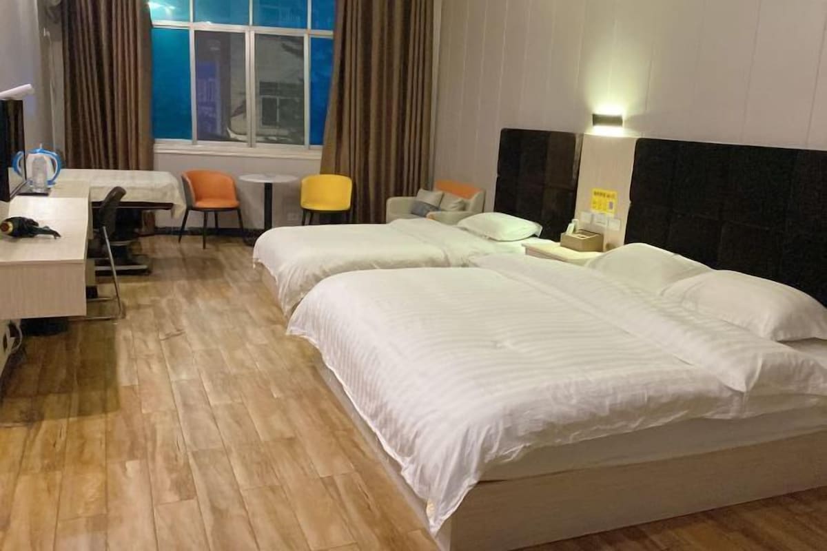 A hotel room with two beds, a desk, a chair, and a small table.