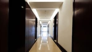 A long, narrow hallway with a reflective floor, flanked by dark-colored walls and doors, leading to a bright exit at the end. - Yi Qiao Hotel (Chengdu)
