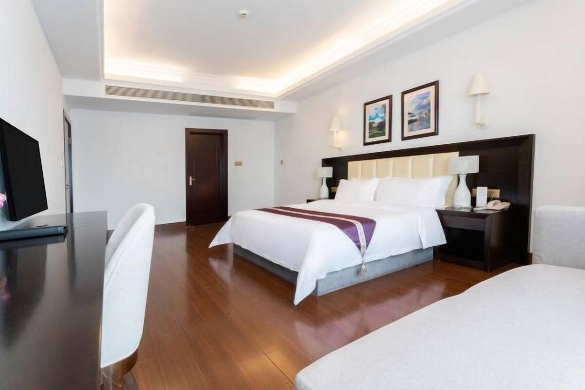 A hotel room with a bed, bedside tables, a desk, a chair, and a television.