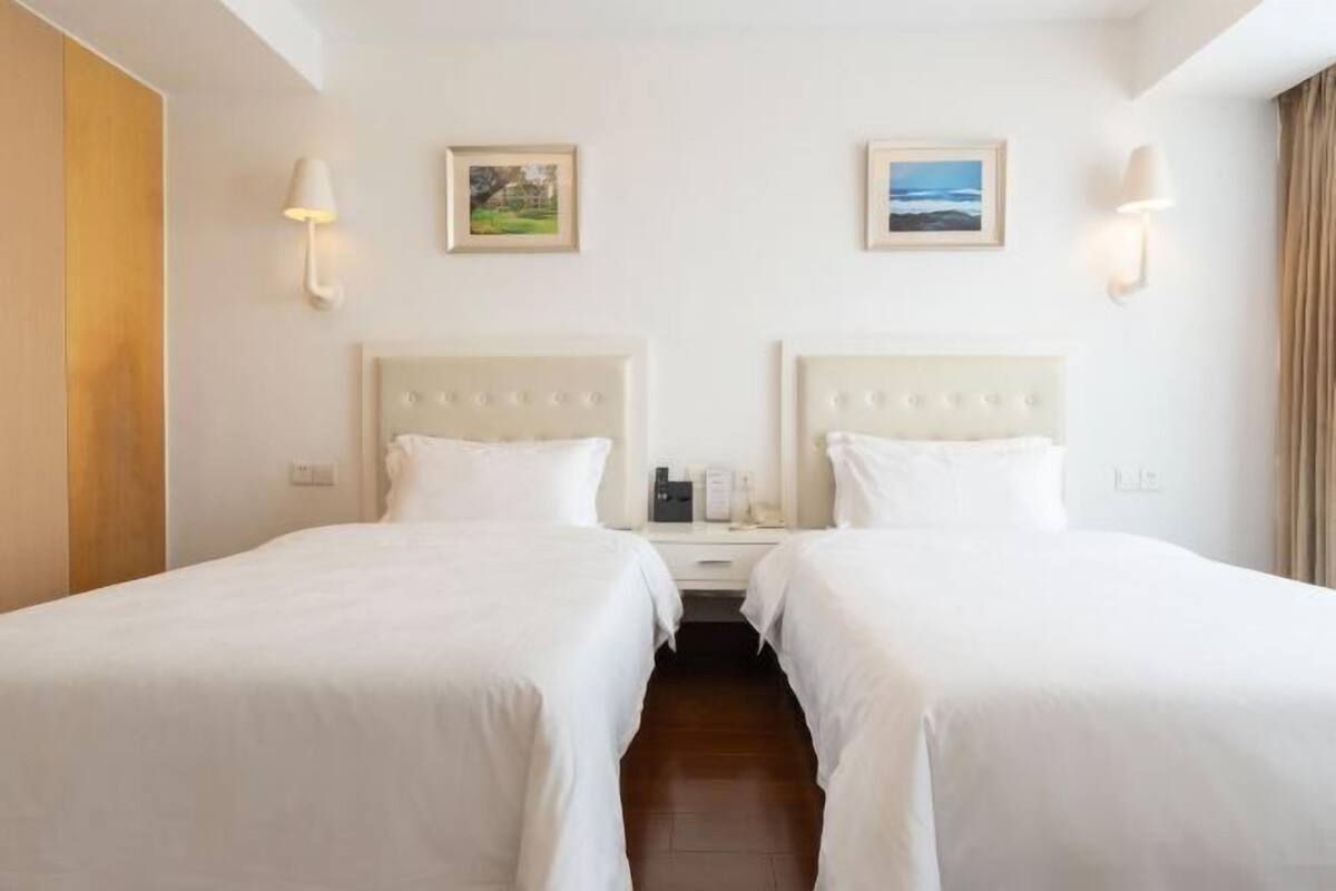 A hotel room with two beds, a wooden wardrobe, a nightstand with a lamp, and two framed pictures on the wall.