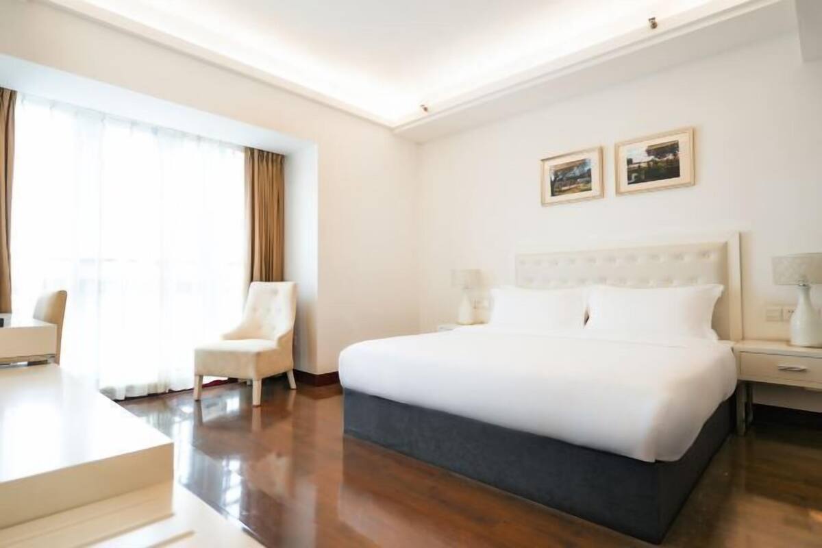 A hotel room with a large bed, a chair, a desk, and a window with curtains.