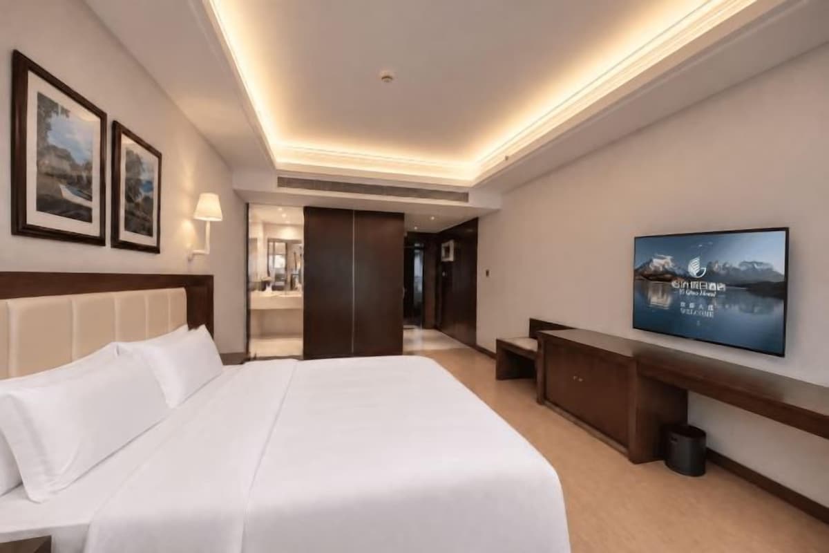 A hotel room with a large bed, a flat-screen TV mounted on the wall, and a desk with a chair.
