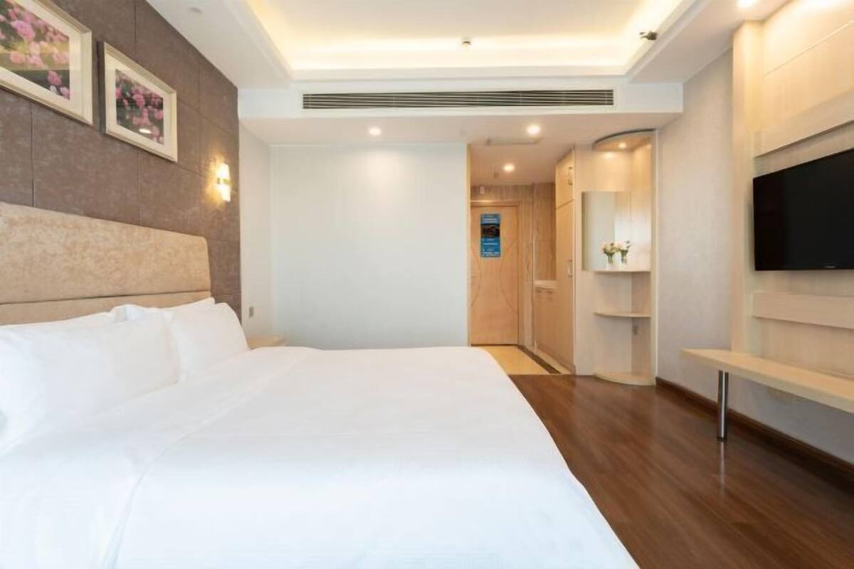 A hotel room with a large bed, a TV mounted on the wall, and a wooden floor.