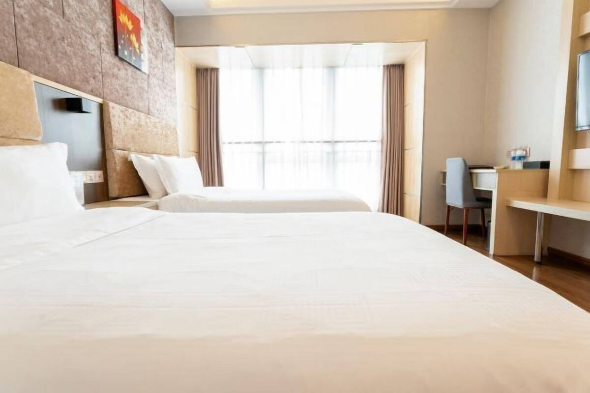 A hotel room with two beds, a desk, a chair, and a large window with curtains.